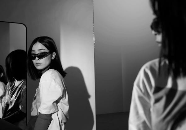 Eine Frau mit Sonnenbrille steht vor einem Spiegel.