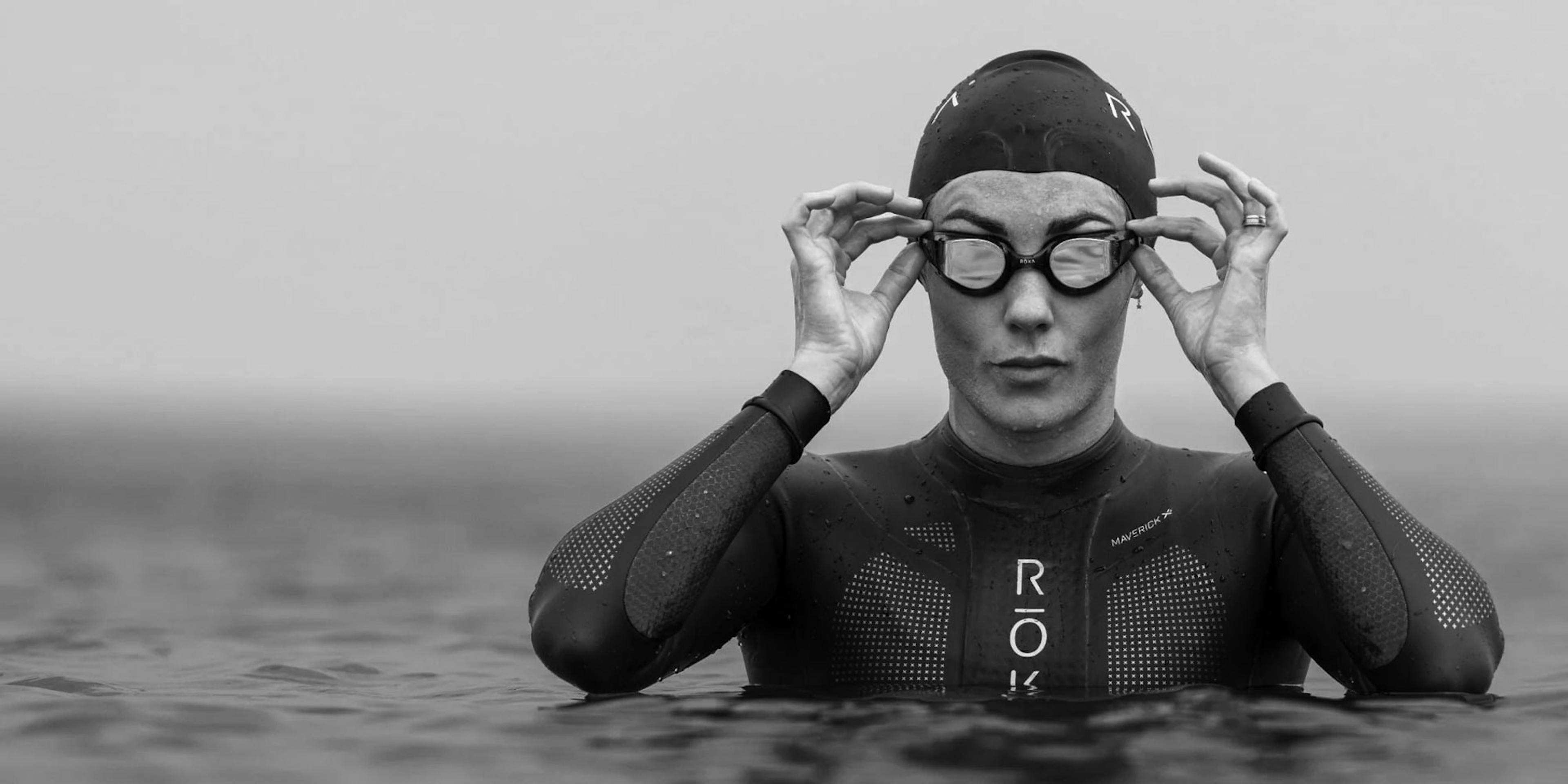 ROKA Multisport athlete wearing a ROKA wetsuit while standing in the water and putting on their goggles.