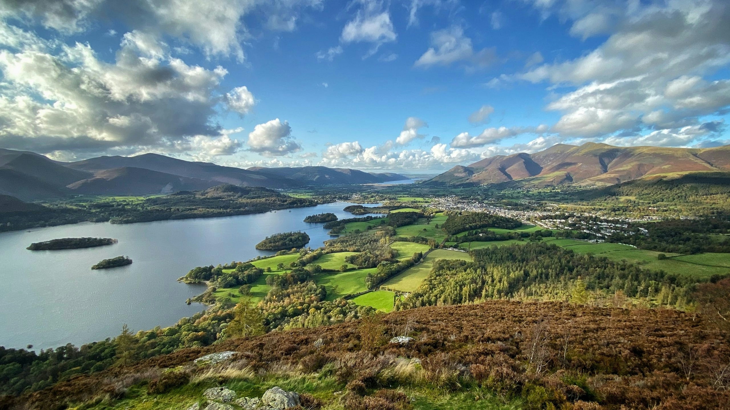 View of lake, surrounded by rich green land with hills in the distance