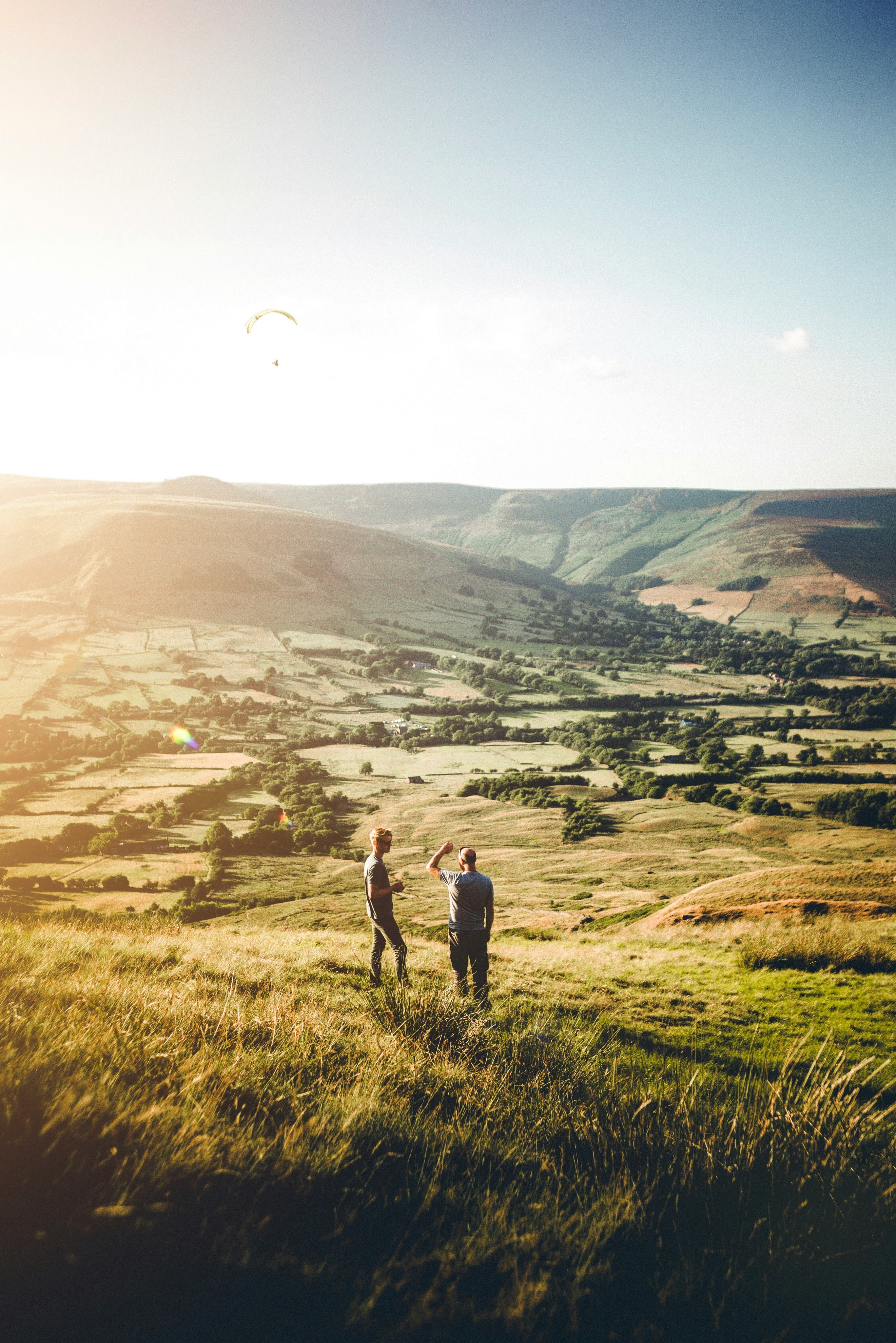 2 people standing on top of a grassy hill with green rolling hills behind