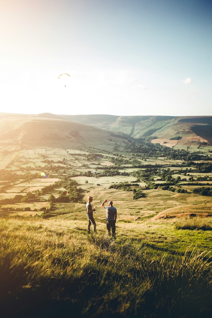 2 people standing on top of a grassy hill with green rolling hills behind