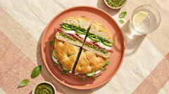 Focaccia-sandwich met pistachepesto, mozzarella, salami en rucola op een koraalroze bord, van bovenaf, in de foodstijl van PLUS (AI-beeld)
