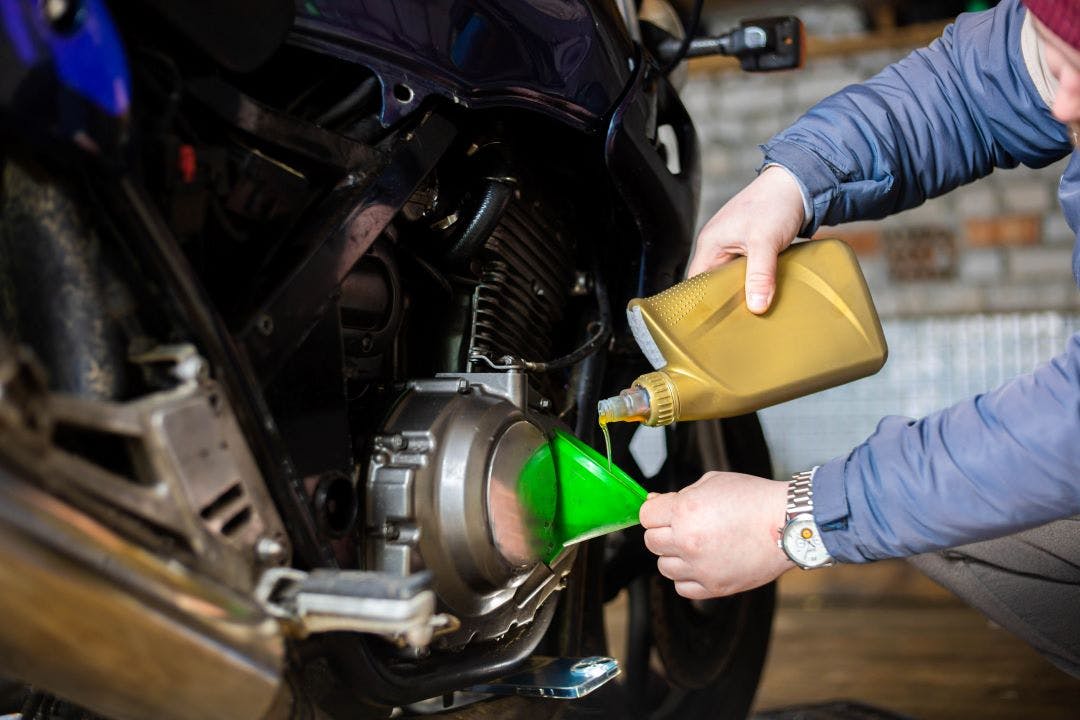 picture of a man putting new oil into his motorcycle after an at home oil change using a funnel DIY motorcycle oil change how to instructions