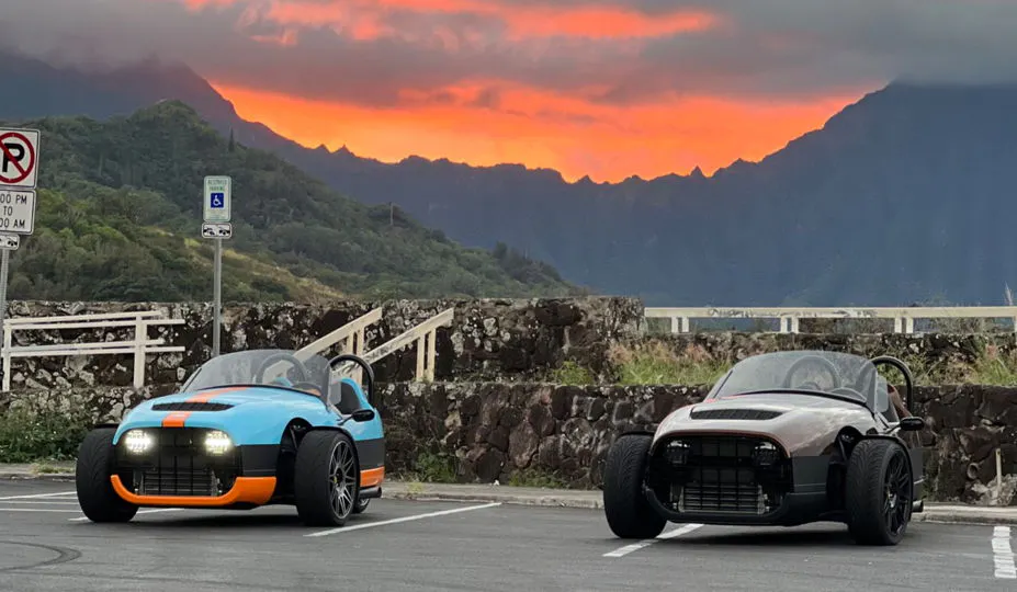 Foto de duas bicicletas motorizadas Vanderhall em um estacionamento no Havaí, com um lindo pôr do sol e montanhas ao fundo