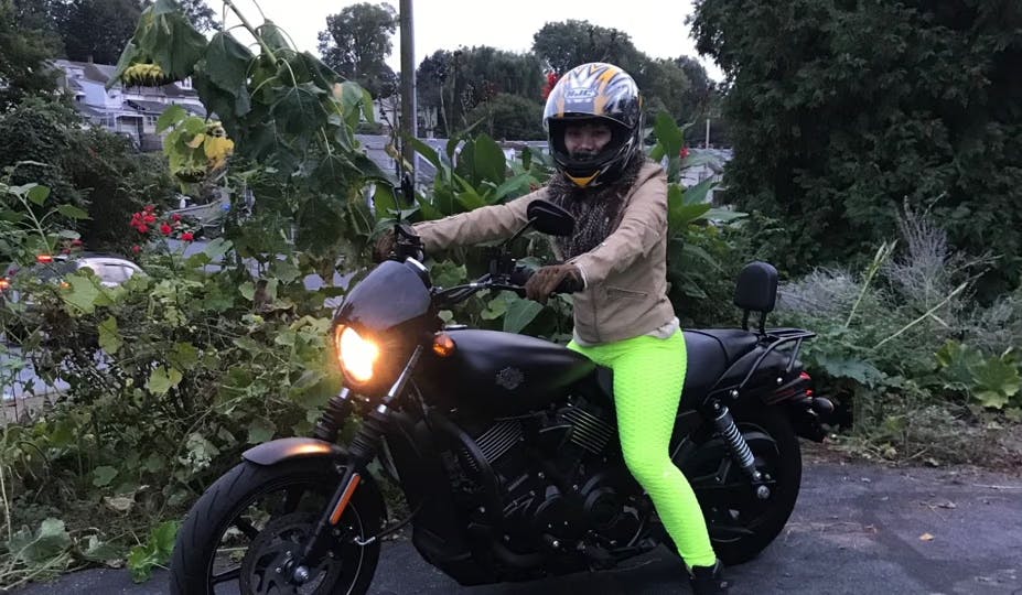 picture of a woman with a helmet sitting on a black harley davidson street 750 with flowers in the background