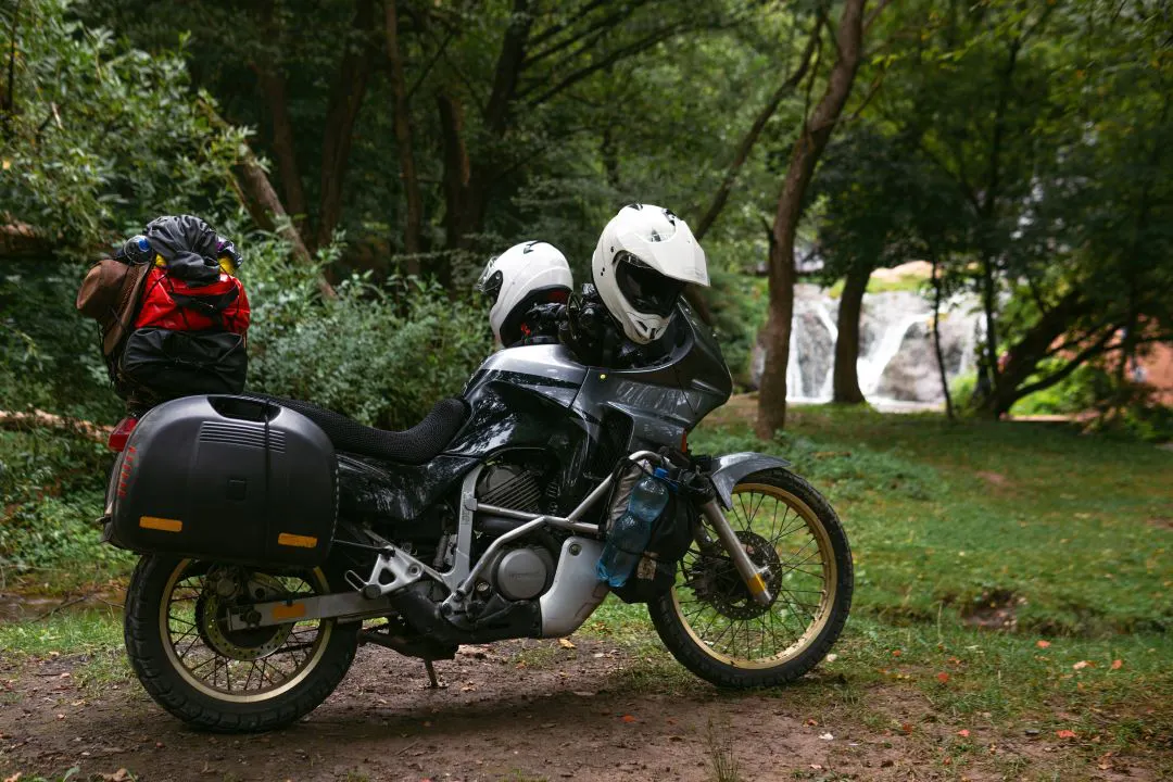 Foto de uma motocicleta com 2 capacetes estacionados ao lado de uma cachoeira, as melhores motocicletas para duas pessoas
