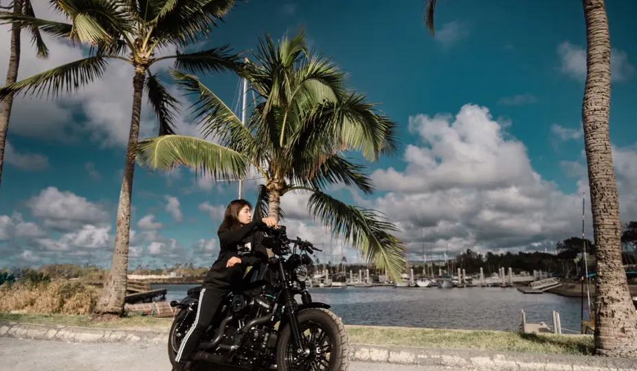 rutas en motocicleta en Hawaii, rutas en motocicleta en Hawaii; mujer en motocicleta en Hawaii cerca del océano junto a palmera