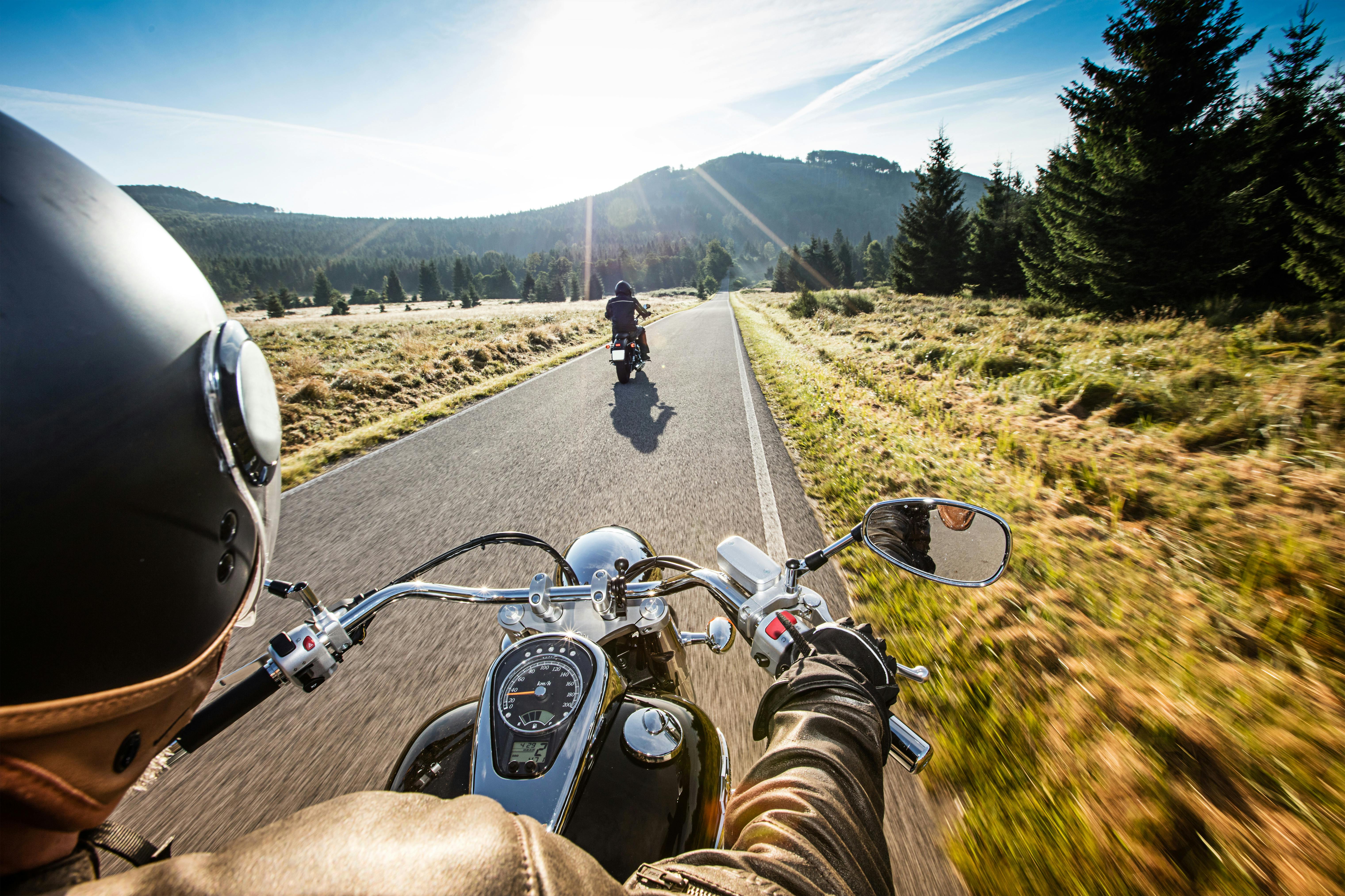 Two people on motorcycles riding on a scenic road through the wilderness on a sunny day