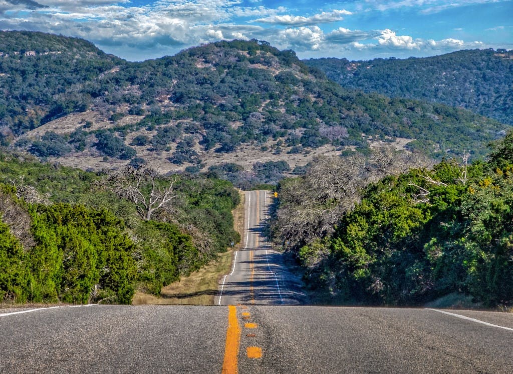 picture of a long road in Texas Hill County with Mountains in the background