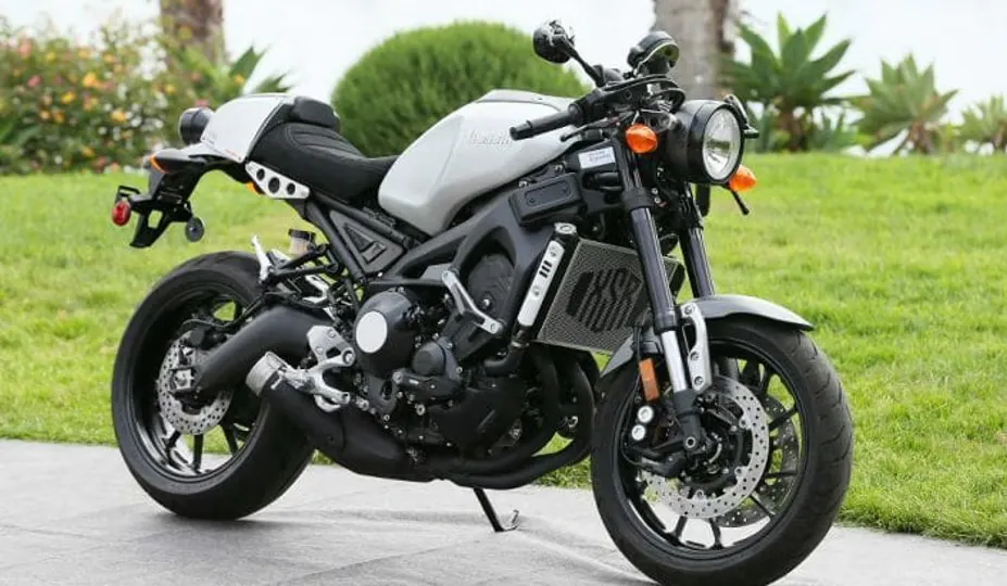 Foto de uma Yamaha XSR900 de 2016 estacionada em frente a uma paisagem gramada com árvores ao fundo