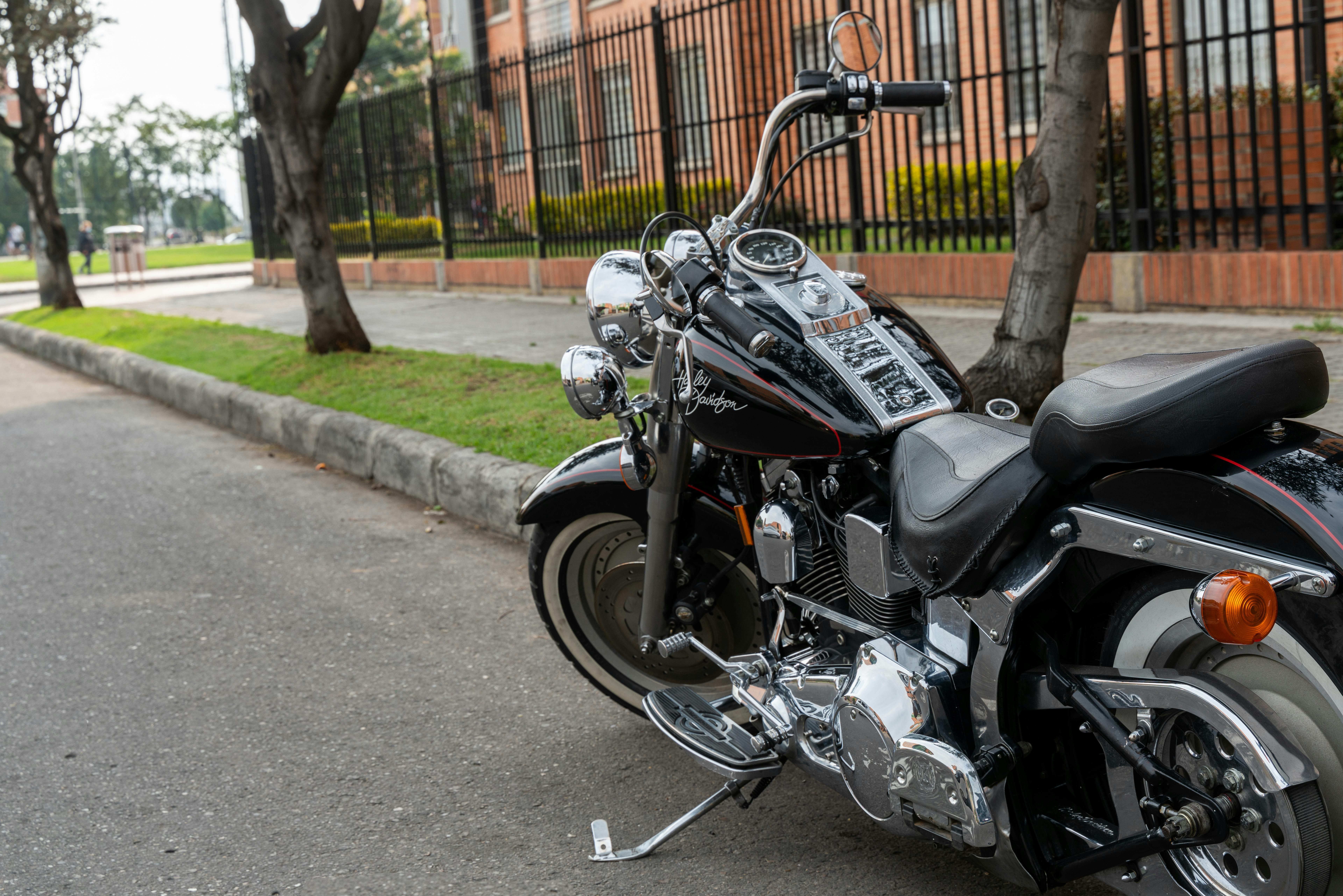 Picture of a black Harley Davidson Fat Boy motorcycle parked on the side of a road in front of a big brick building