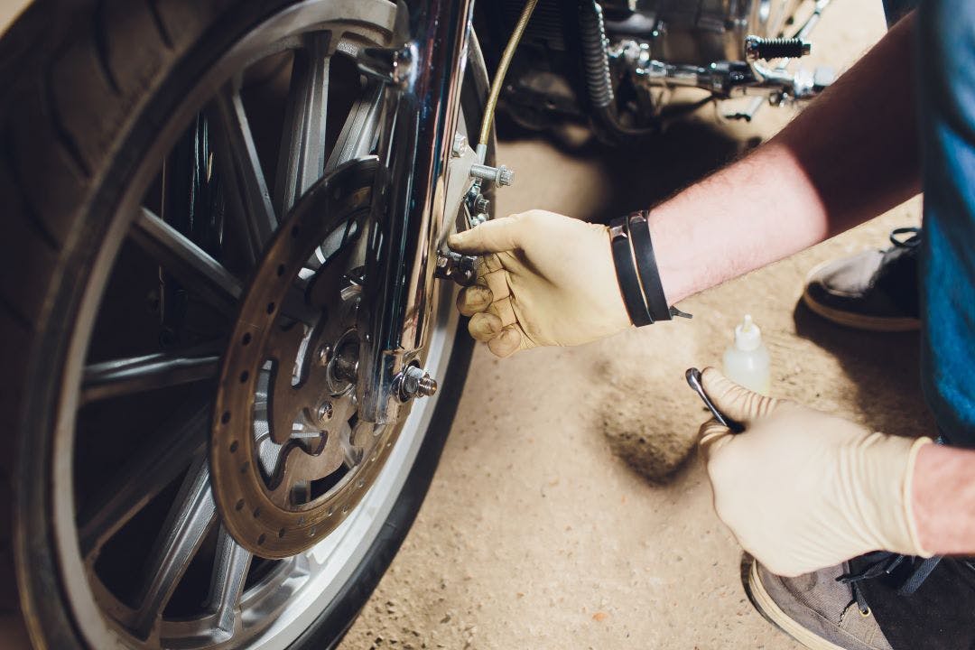 man checking his motorcycle brakes as part of a monthly motorcycle maintenance checklist to ensure safe riding DIY motorcycle maintenance