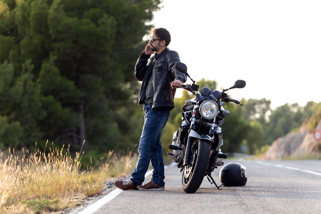 Man biker talking on the phone to the insurance of his motorcycle after having suffered a breakdown on the road. How Much is Motorcycle Insurance? What to Expect