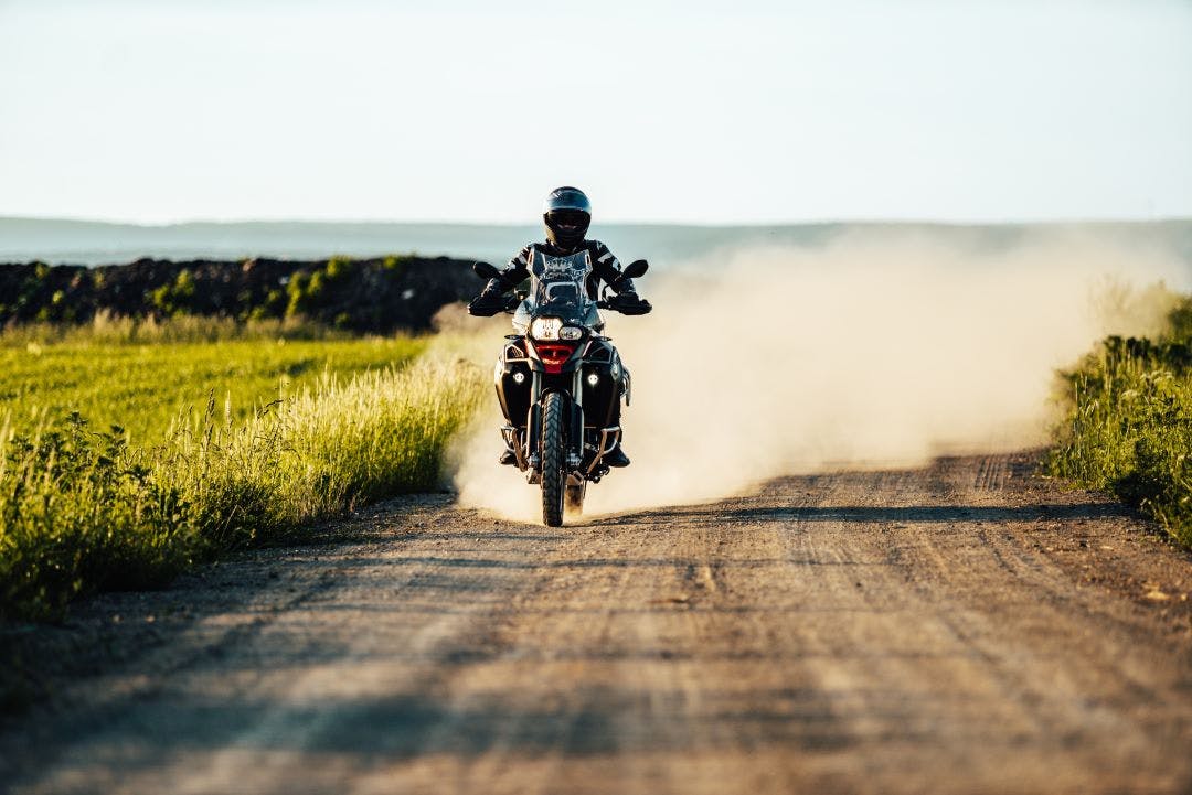 person on motorbike riding on dirt road with cloud of dust pros and cons of owning multiple bikes