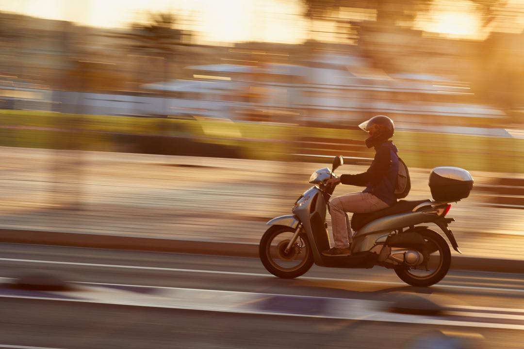moped driving on road Vespa vs. Moped: What's the Big Difference?