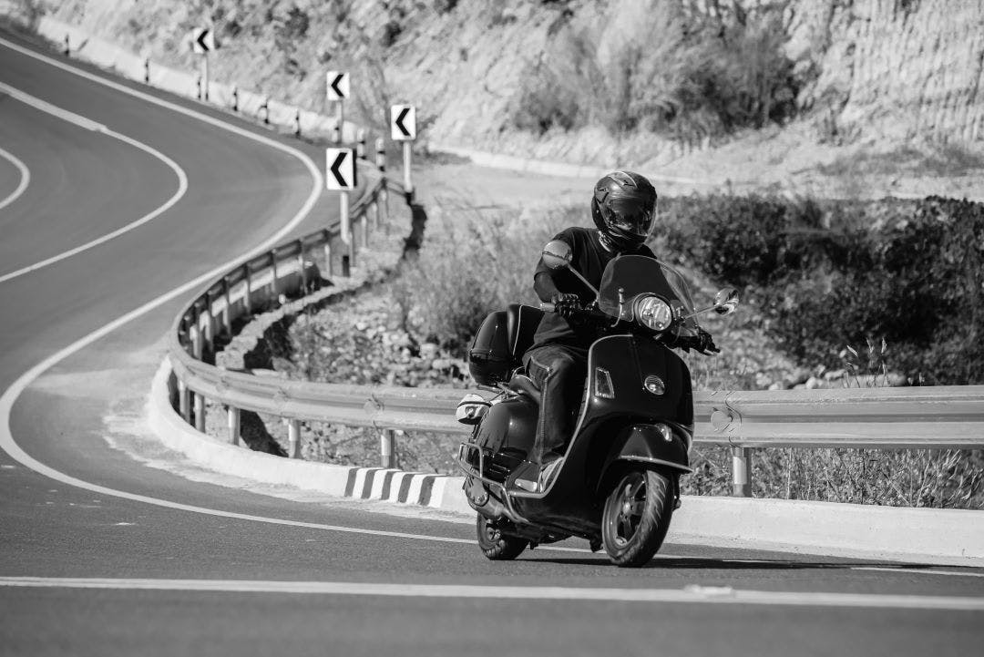 black and white picture of a vespa on a curvy road Can Vespas Go On the Highway? Vespa Riding FAQs