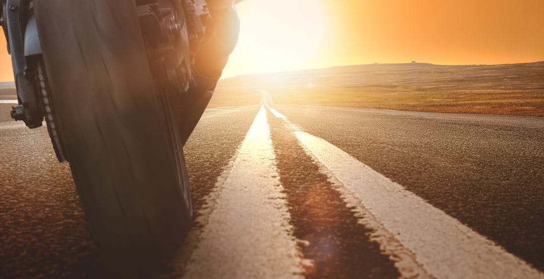 motorcycle driving towards sun on empty road How to Stay Cool Riding a Motorcycle in the Summer