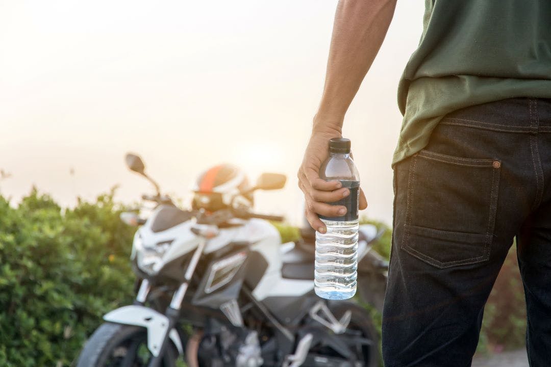 man holding water bottle with bike in background How to Stay Cool Riding a Motorcycle in the Summer