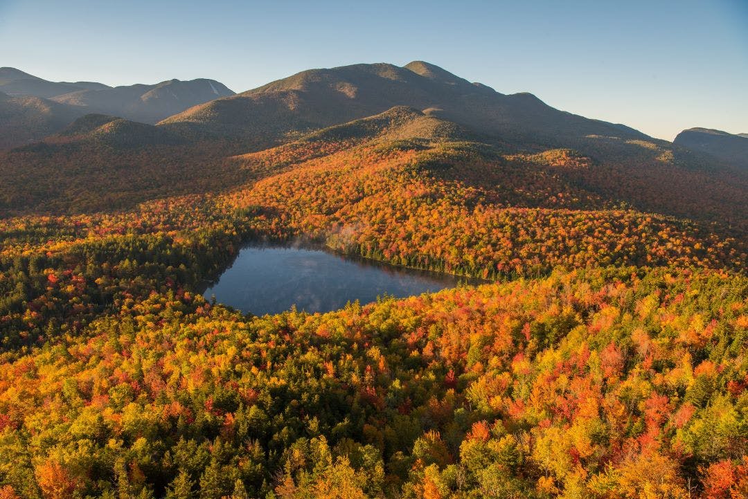 Morning light illuminates the fall color in the Adirondack Mountains over Heart Lake Best End of Summer Motorcycle Destinations to Plan ASAP