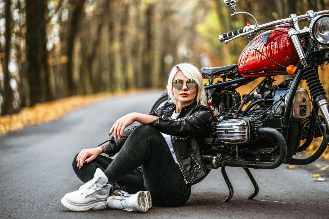 Pretty blonde biker girl in sunglasses sitting near red motorcycle on the road Badass Women's Motorcycle Clubs & Collectives