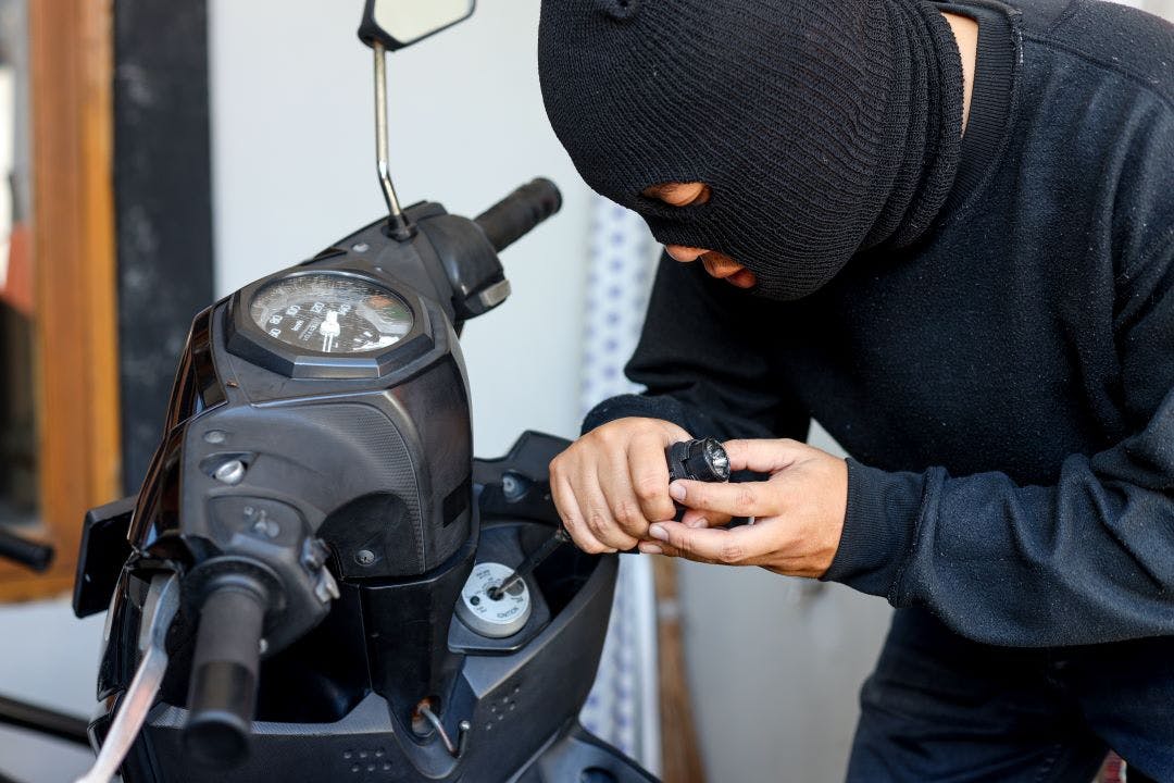 Motorcycle thief in black mask trying to unlock the ignition key of motorcycle with screwdriver. Street criminal, crime and people concept Motorcycle Rental Insurance: How Does It Work?