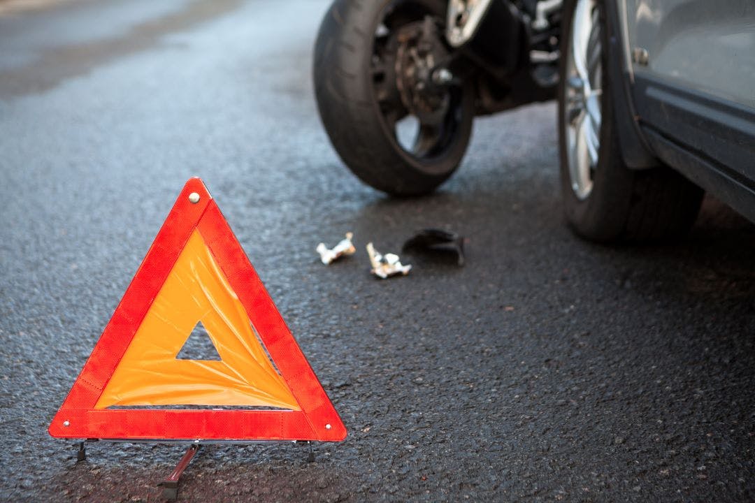 Emergency warning triangle positioned on asphalt road due accident with a motorcycle and a car Here's What to Do After a Motorcycle Accident on a Rental