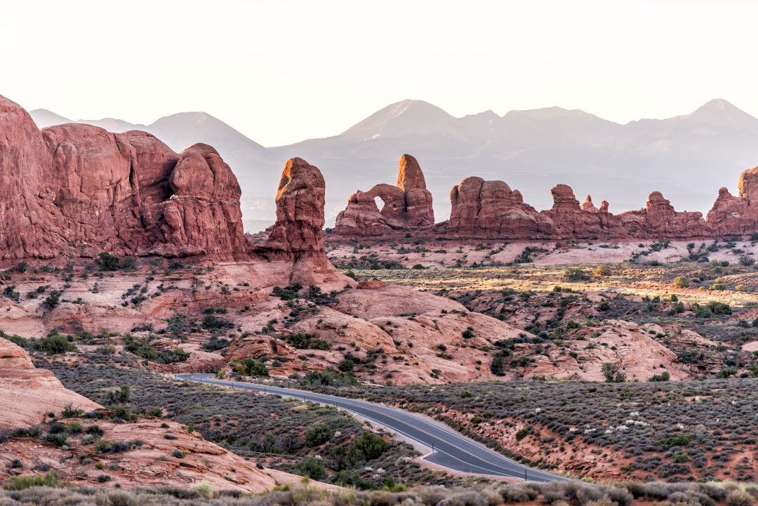 High angle aerial view of road leading to window arch in Arches National Park in Utah during morning sunrise with orange red pink rock color Best of Utah Motorcycle Rides to Explore Now