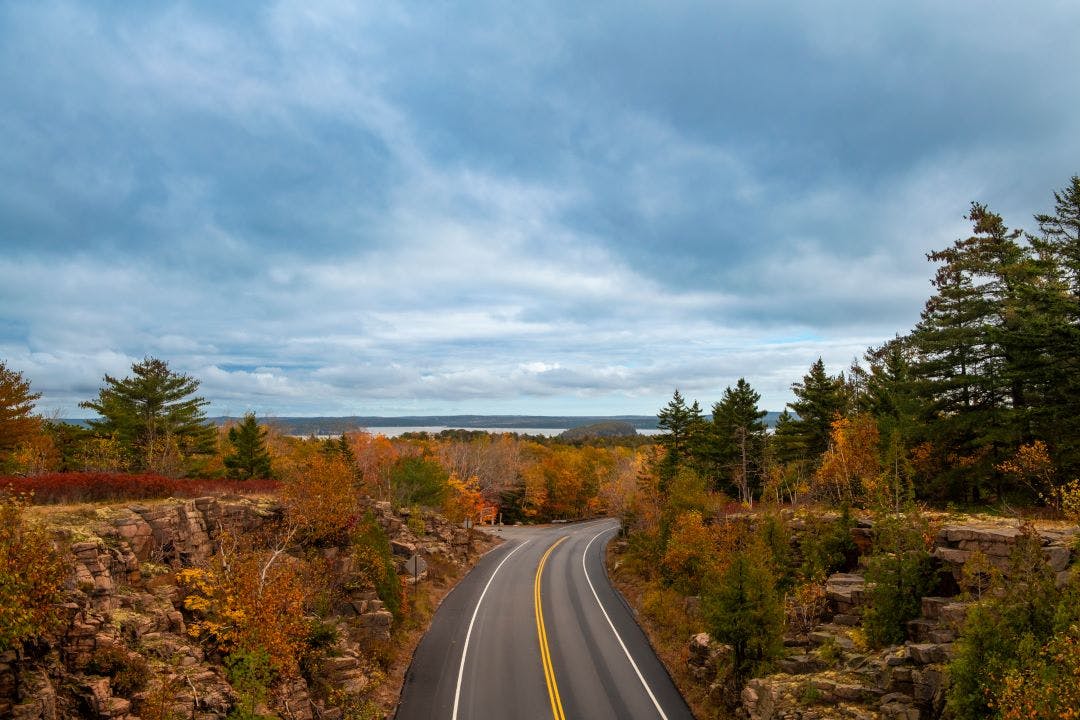 Scenic road along the Acadia National Park, Maine, USA, with the autumn foliage colors and the sea on the background 10 Most Memorable Self-Guided Motorcycle Tours in the USA