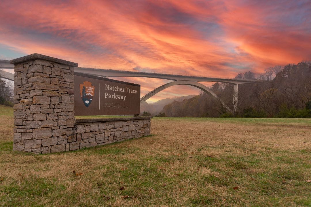 Natchez Trace Parkway Double Arch Bridge. National Park Service sign with arrowhead logo. Dramatic sunset sky. Nashville to New Orleans via Natchez Trace Parkway