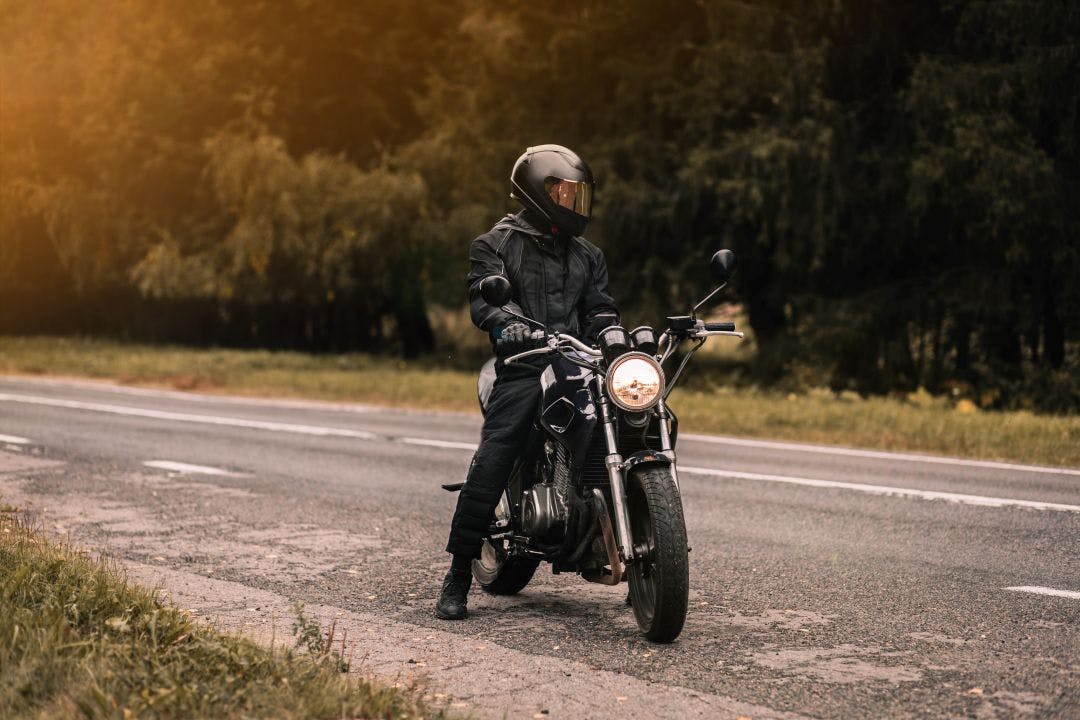 male motorcyclist in a warm jacket and helmet in cold autumn weather on the road with a motorcycle cafe Riding Gear by Season: What You Should Wear & When