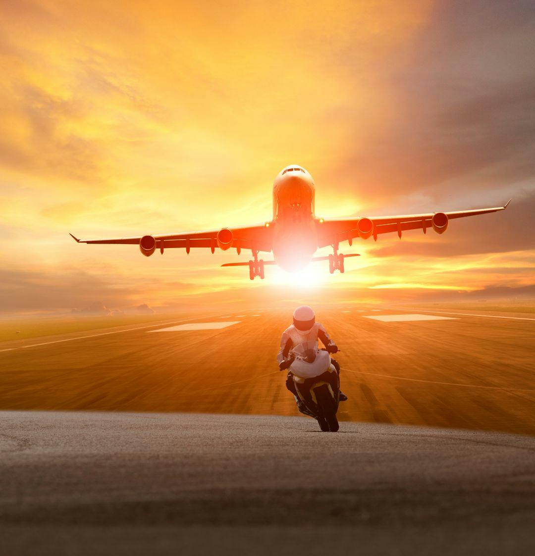 man riding motorcycle on road and plane take off from airport runway background How to Travel With Your Motorcycle Gear on a Plane