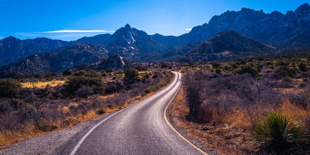 Organ Mountains, Desert Peaks National Monument in Las Cruces, Doña Ana County, New Mexico, Southwestern USA, curved single lane paved road to Sugarloaf Peak through arid desert valley meadow at dusk Beat the Cold With These Winter Motorcycle Destinations