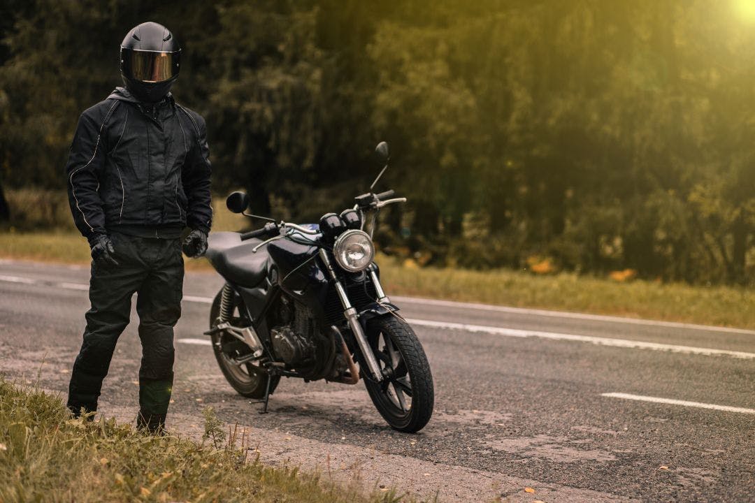 male motorcyclist in a warm jacket and helmet in cold autumn weather on the road with a motorcycle cafe racer How to Stay Warm on a Motorcycle