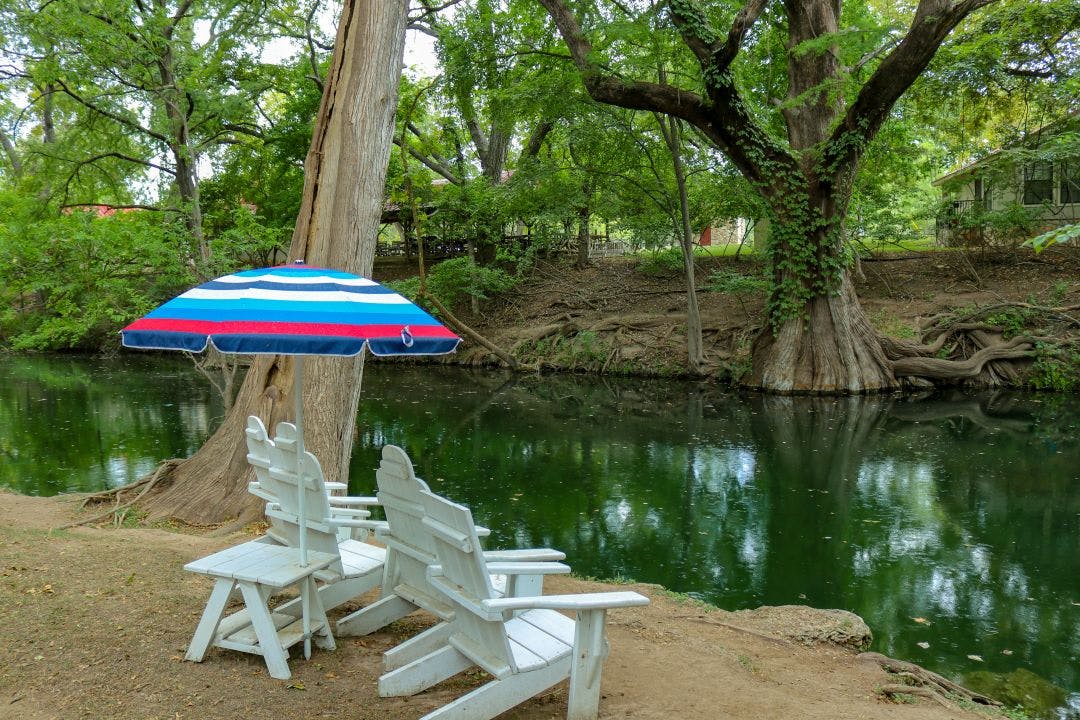 White adirondack lounge chairs and a colorful sun umbrella for relaxing on a summer day at Cypress Creek a public park Best 15 Day Trips from San Antonio, Texas