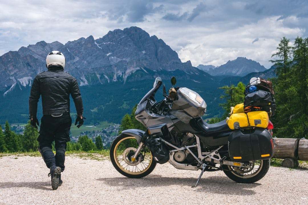 Back view of biker with adventure touring motorcycle in full equipment on dirt road, High top mountains on background, tourism travel concept, copy space. world riders Compare Renting a Motorcycle For a Day Vs. Week