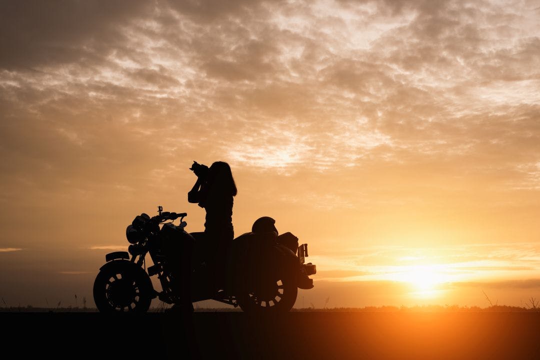 Silhouette of young woman biker take photo and motorcycle on the street at sunrise.Motorbike travel concept Motorcycle Rentals & the Gender Gap – Improving Equity