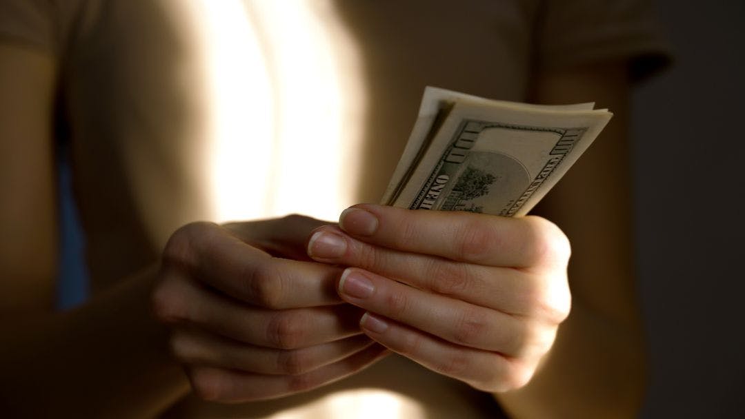 A person carefully counts several bills in soft, natural light. The focus is on the hands and cash, creating a serene atmosphere of financial management How to List a Motorcycle Tour on Riders Share & Make Money