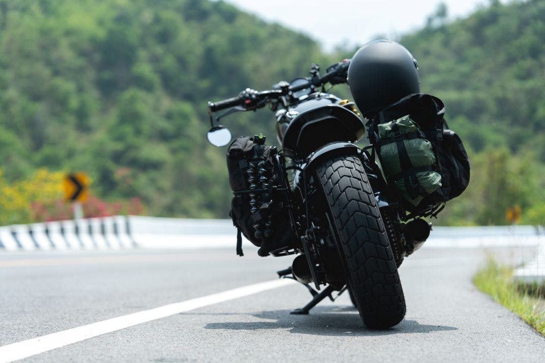 A motorcycle with gear parked on an open road surrounded by green hills and a curving highway Where Should You Tour Next? 5 Motorcycle Tours to Plan Now
