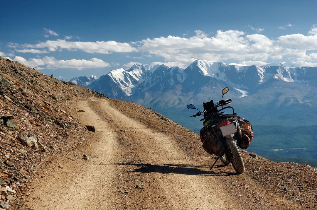 Motorcycle enduro traveler with suitcases standing alone on yellow stone extreme road path on the background of high snow glacier ranges 11 Best Adventure Bikes on the Market Now & Why