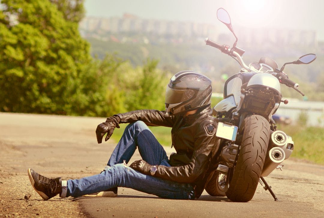 biker sits next to motorcycle on the road during a sunny summer day Best Time to Rent a Motorcycle: Seasonal Trends & Pricing