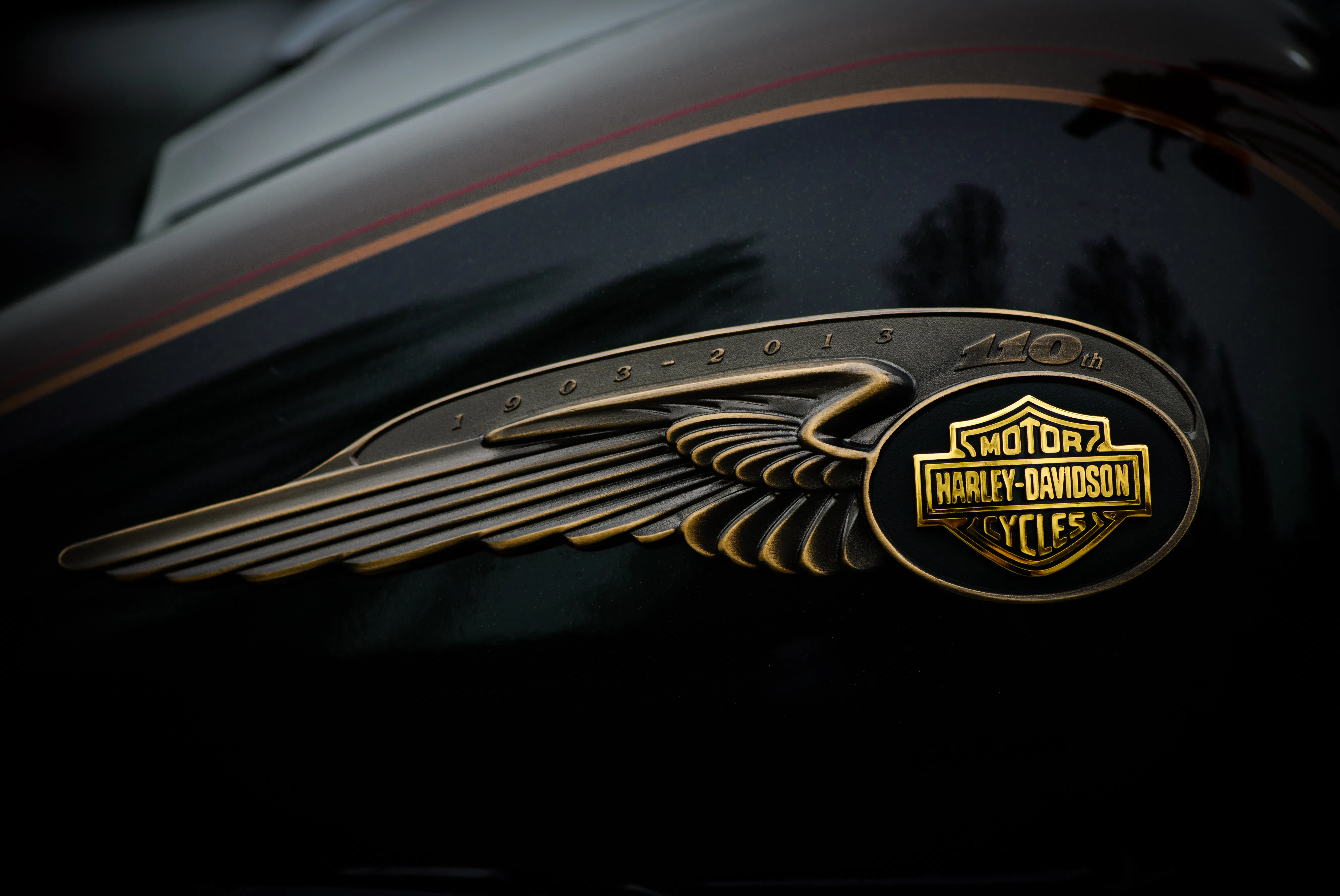 Foto do tanque de gasolina em uma Harley Davidson preta e marrom com emblema do centésimo primeiro aniversário