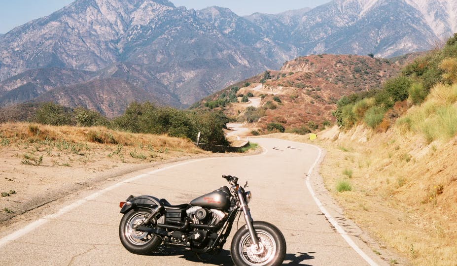 Picture of a harley davidson street bob parked in the middle of a deserted road with mountains in the background