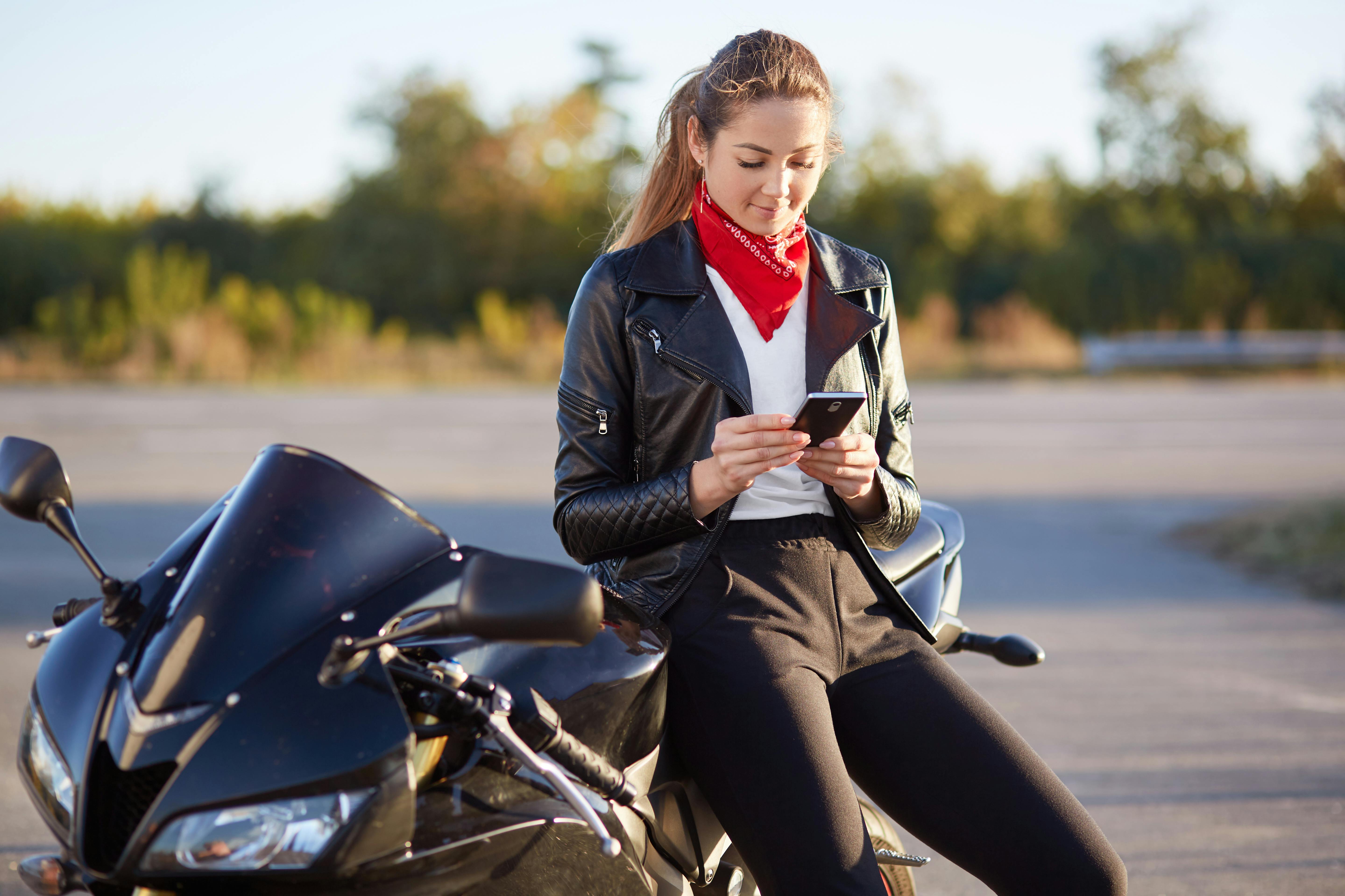 Female motorcycle rider holds smart phone in hands planning her route on a modern mobile app