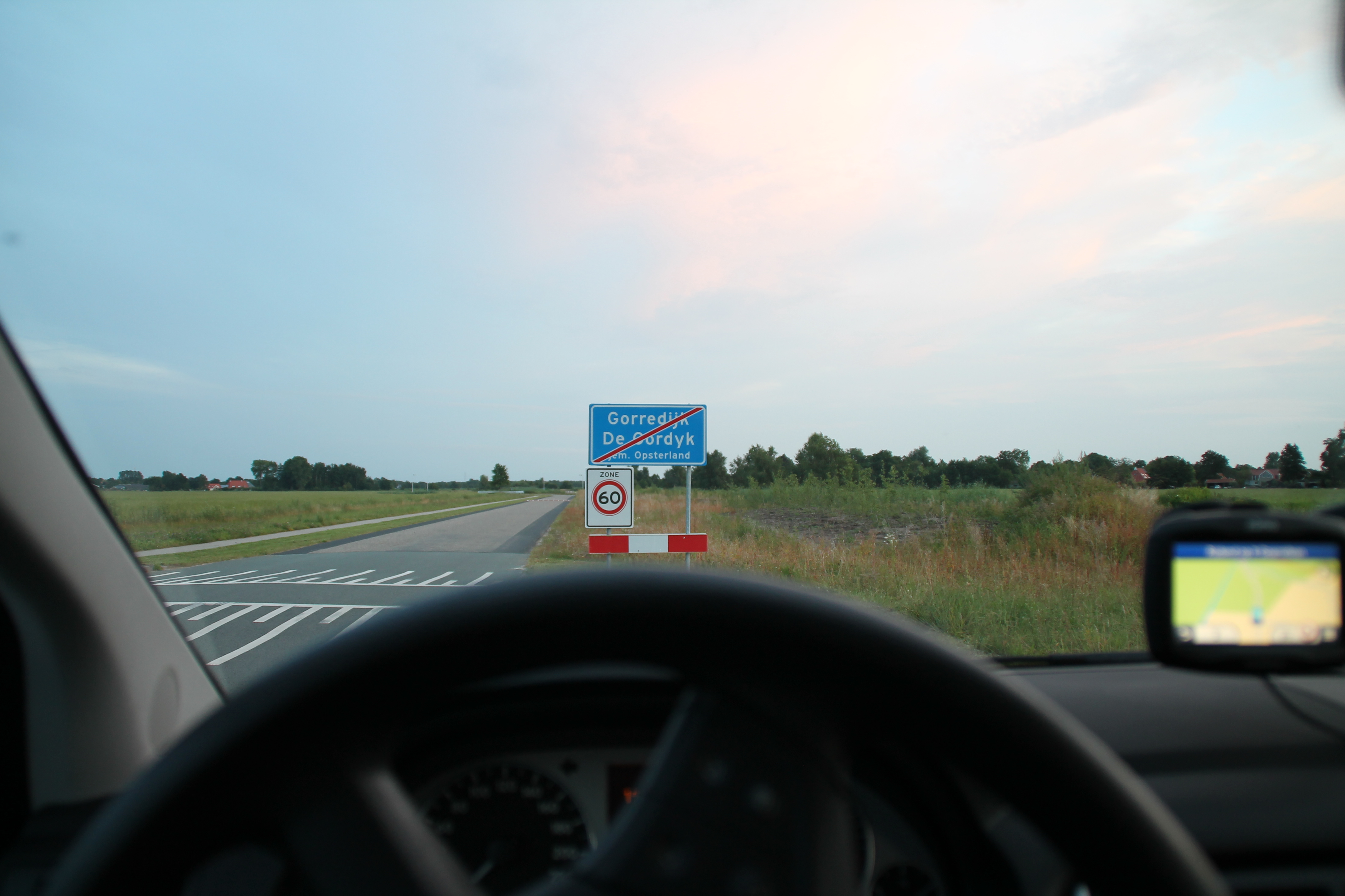Foto over het stuur van de lesauto genomen met in de verte het mooie Friese landschap en het "einde bebouwde kom" verkeersbord van Gorredijk 