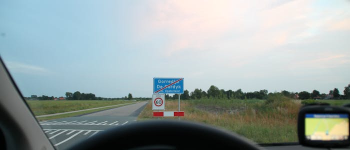 Foto over het stuur van de lesauto genomen met in de verte het mooie Friese landschap en het "einde bebouwde kom" verkeersbord van Gorredijk 
