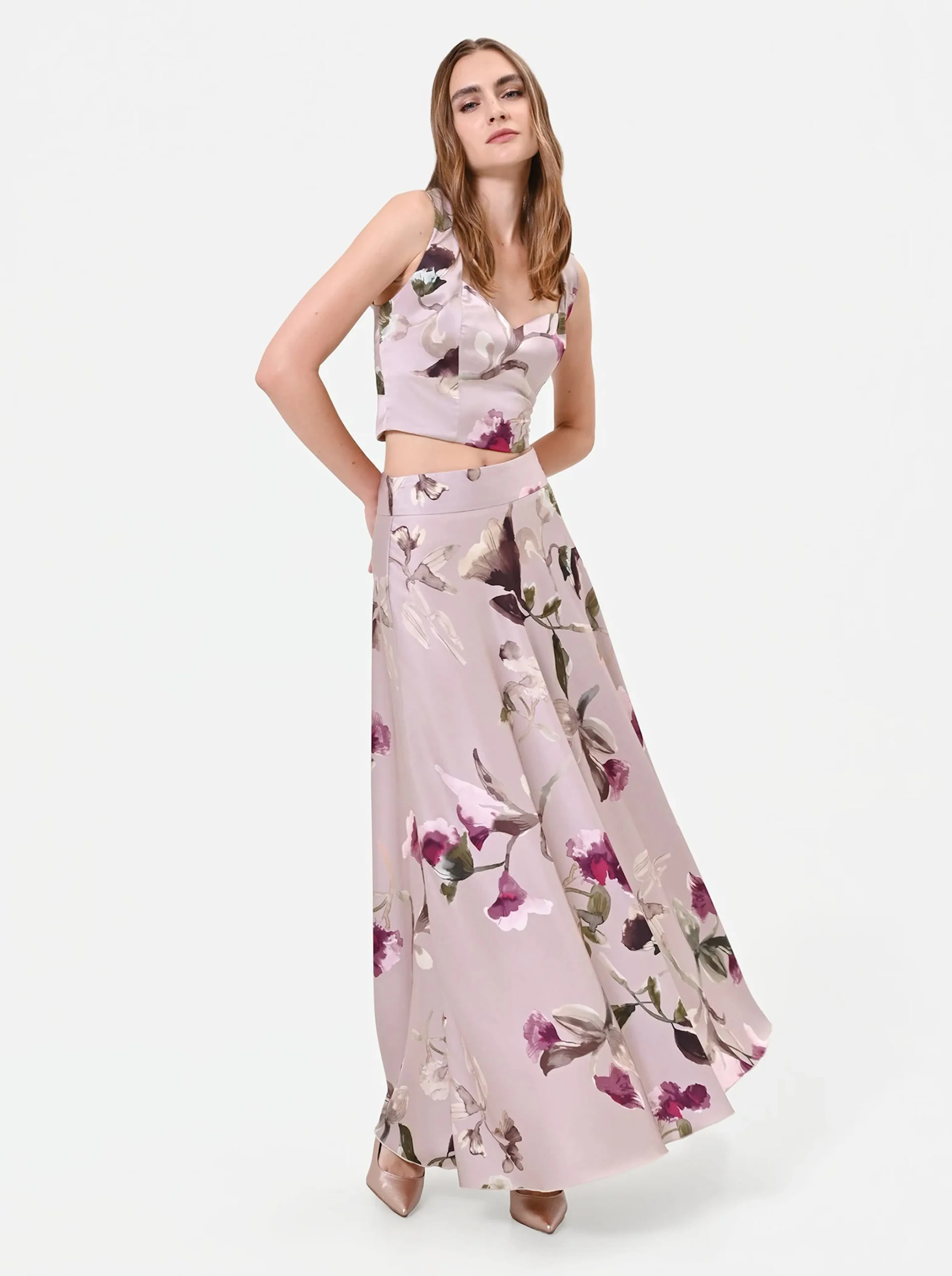 Woman in a sleeveless floral crop top and matching flowy long skirt with pink and purple flowers, posing confidently against a plain white backdrop.