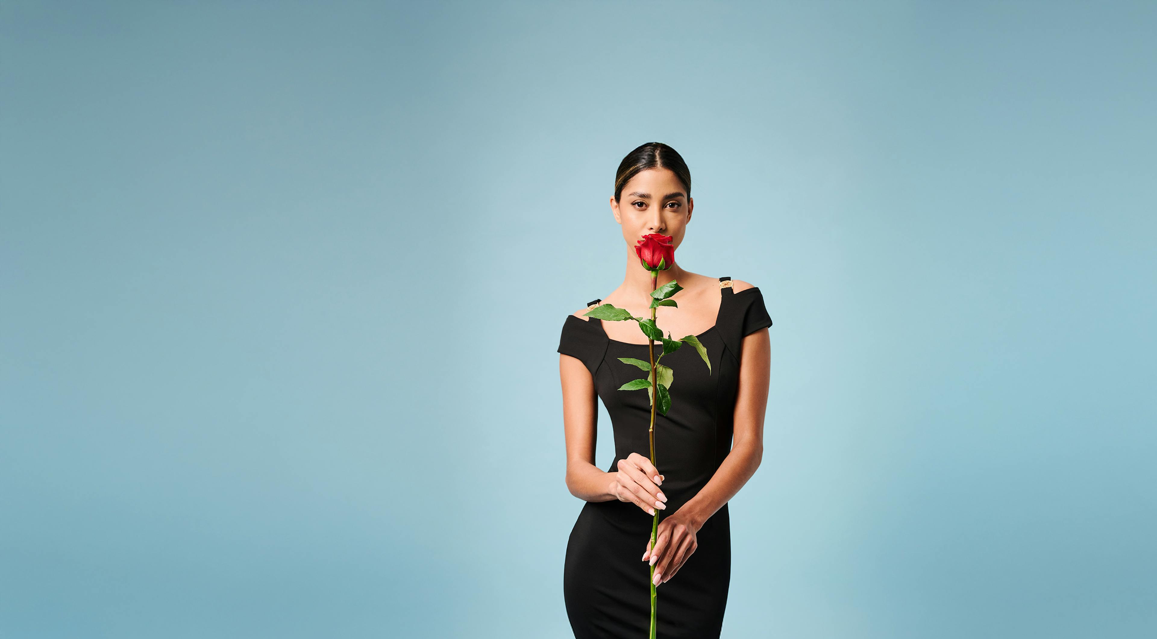 A woman in a stylish black dress stands holding a rose