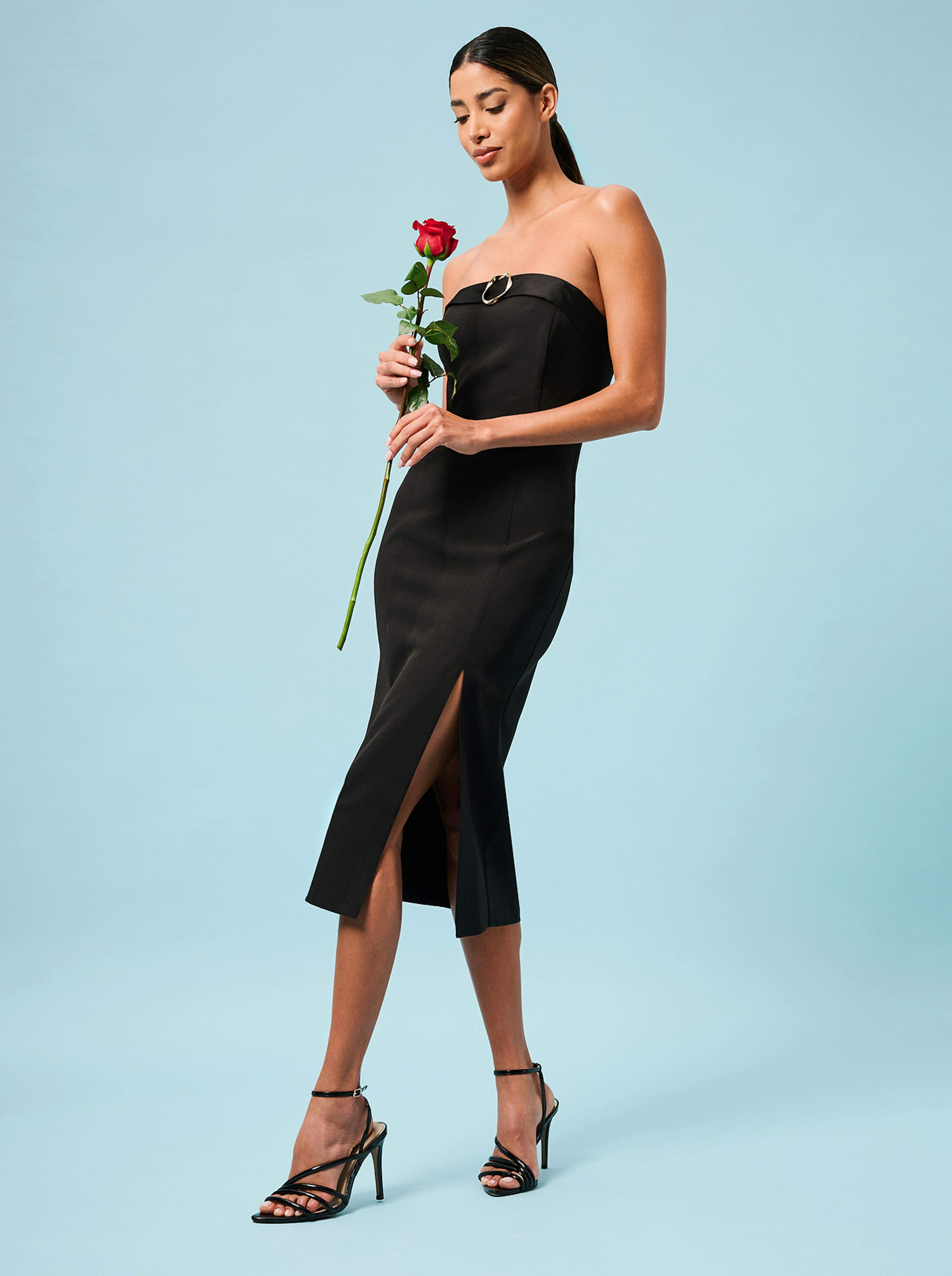 A woman in a black midi dress gracefully holds a single rose