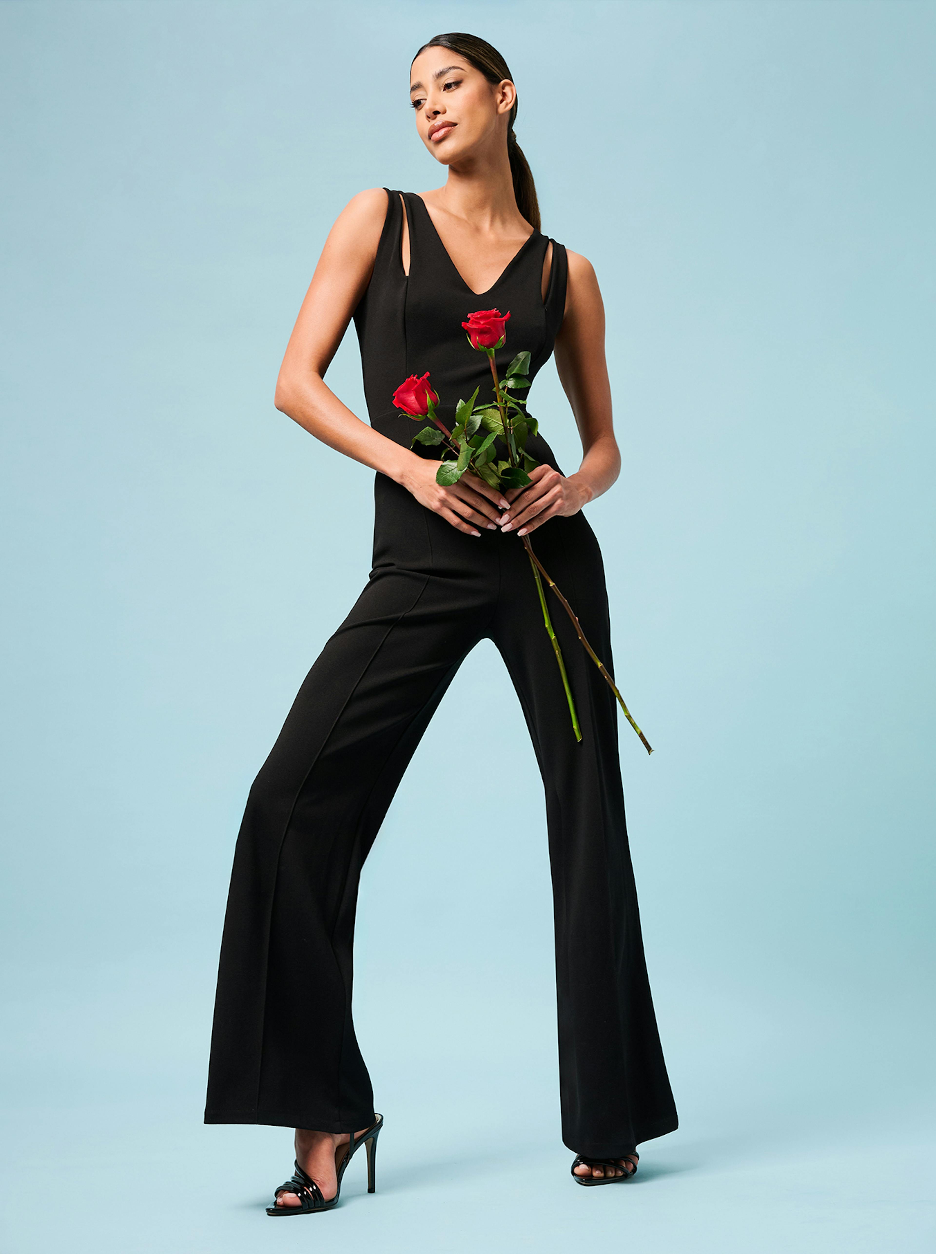 A woman in a black jumpsuit gracefully holds two roses