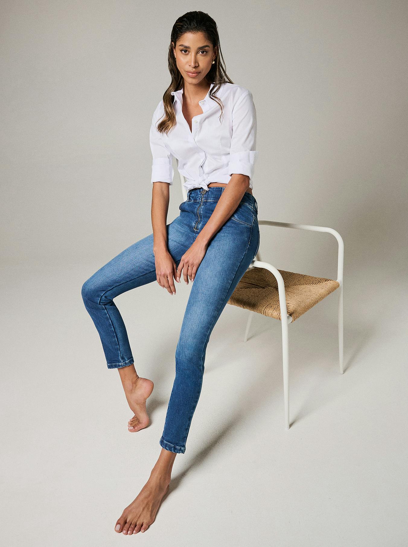 A woman in jeans and a white shirt sits comfortably on a chair